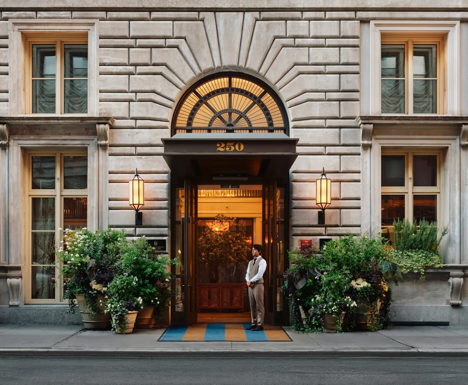 The arched door of The Fifth Avenue Hotel’s mansion at 250 Fifth Avenue, a doorman between the plants