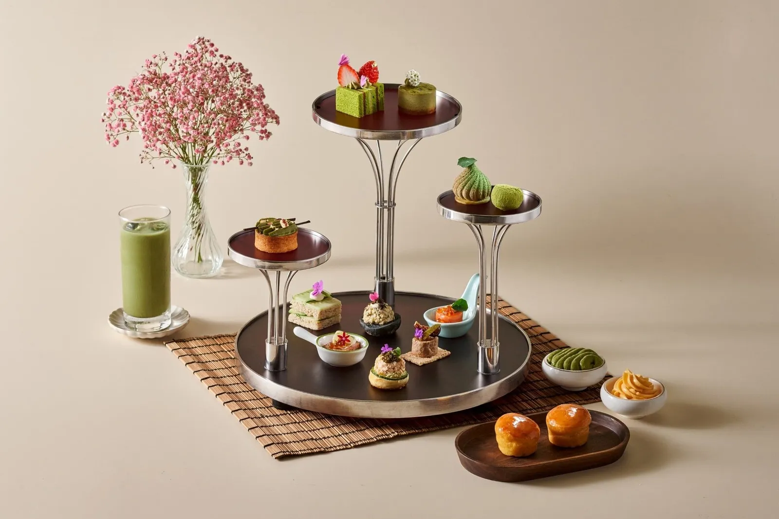 An afternoon tea stand of green matcha pastries, with a glass of matcha and a spray of pink flowers.