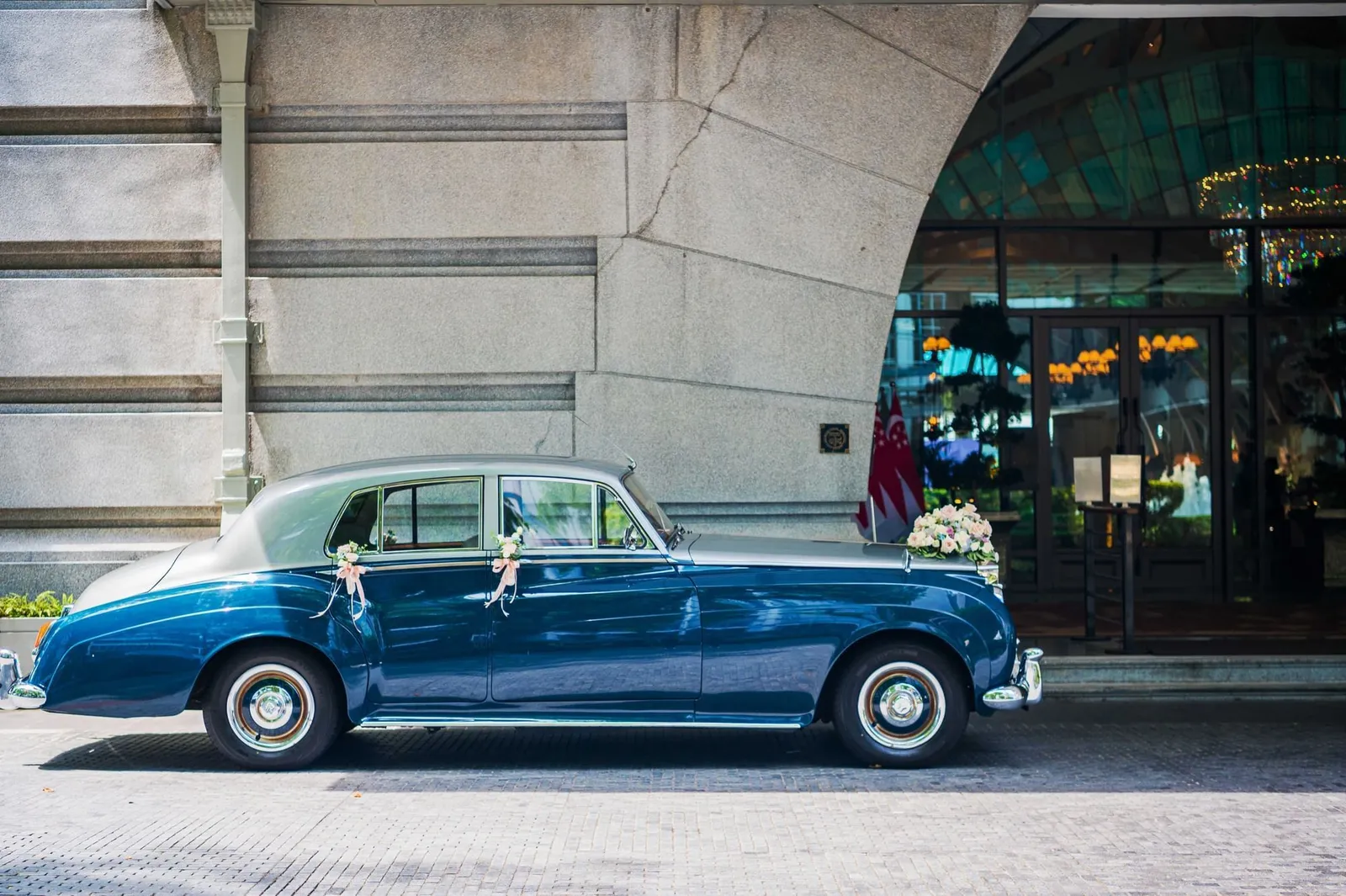 A vintage blue Rolls-Royce with wedding ribbons, parked in front of Clifford Pier’s entrance arch.