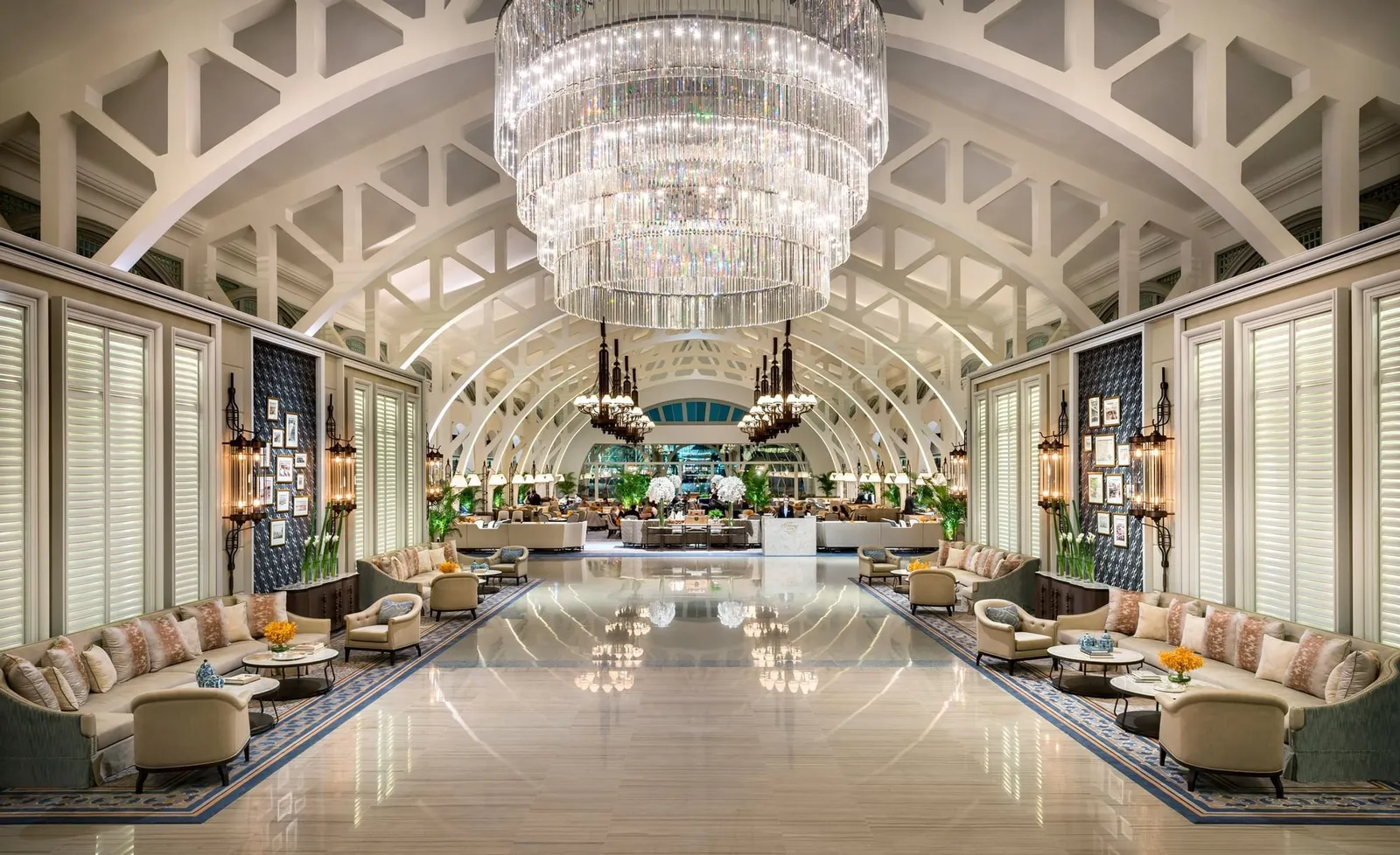 The arrival hall: white arched trusses overhead, a large crystal chandelier and sofas along both sides.