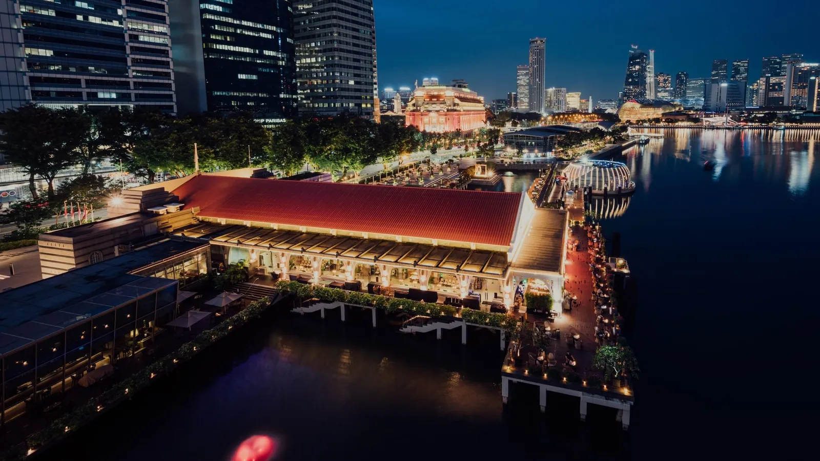 Clifford Pier from above at night: the long red-tiled roof over the water, its lit veranda and the lights around the bay.