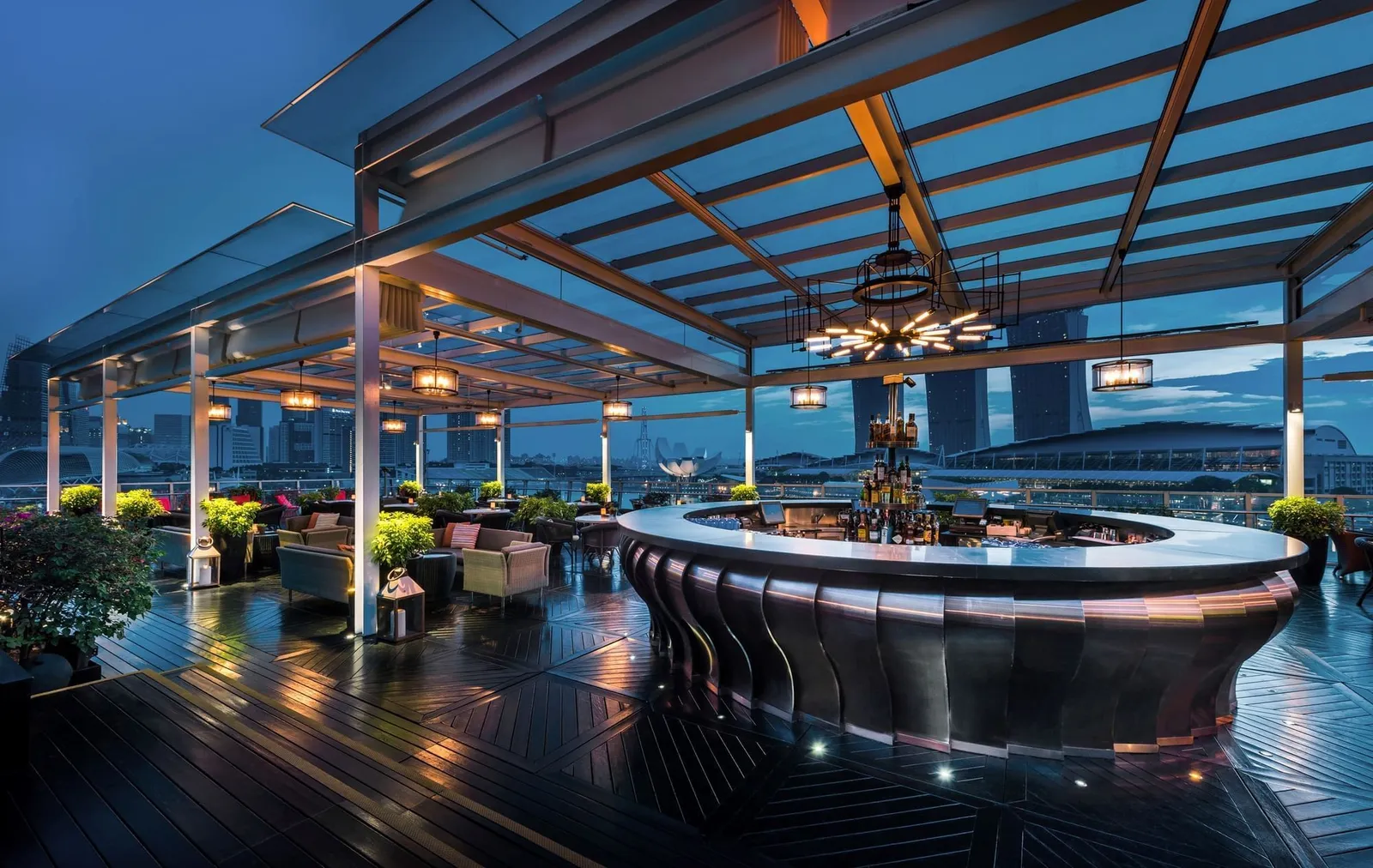Lantern’s circular bar counter at dusk under its glass canopy, with sofas around it and the towers of Marina Bay Sands behind.