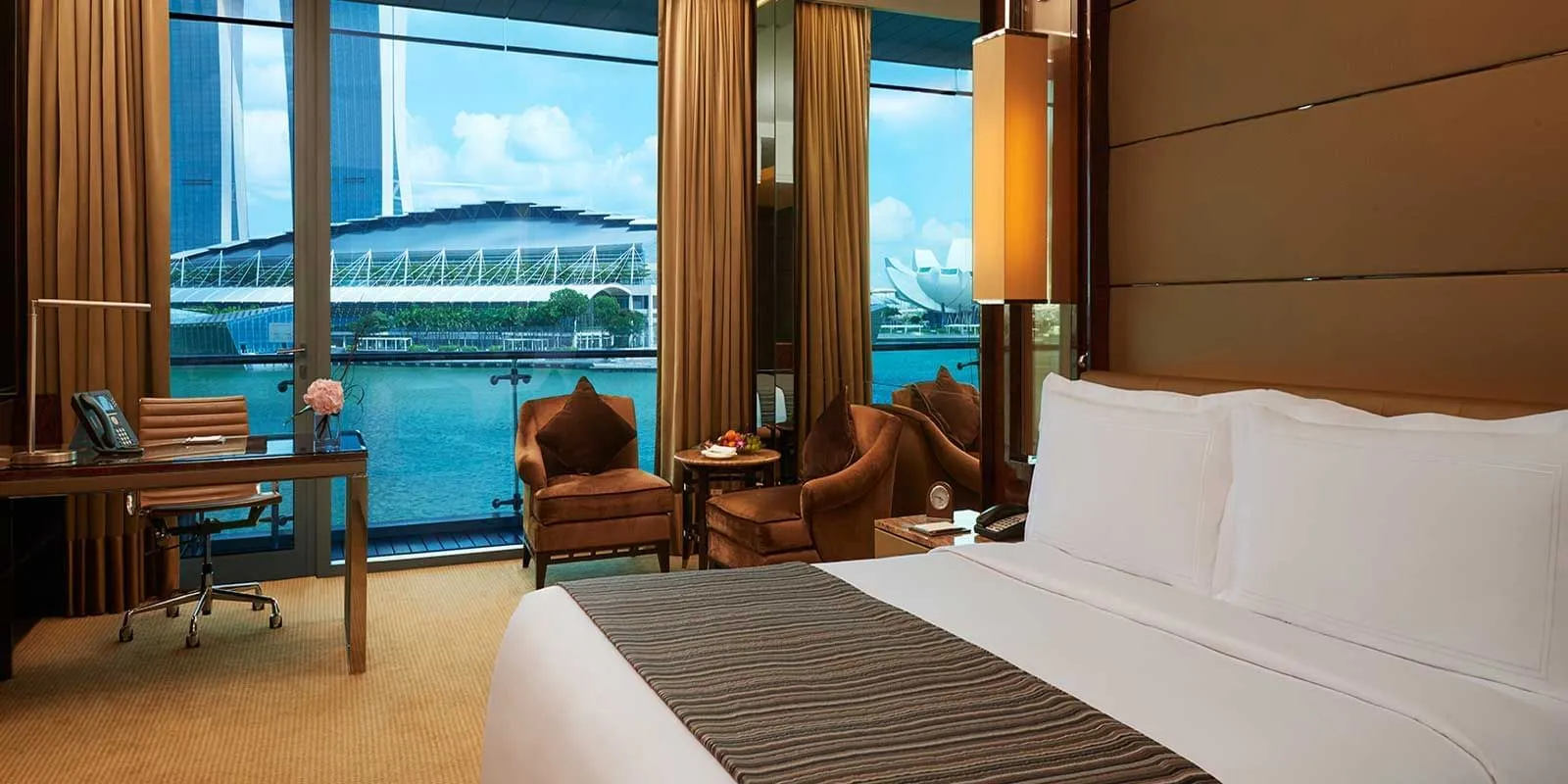 A Bay View Room: the bed in the foreground, the desk and armchairs by the window, with the water of the bay outside.