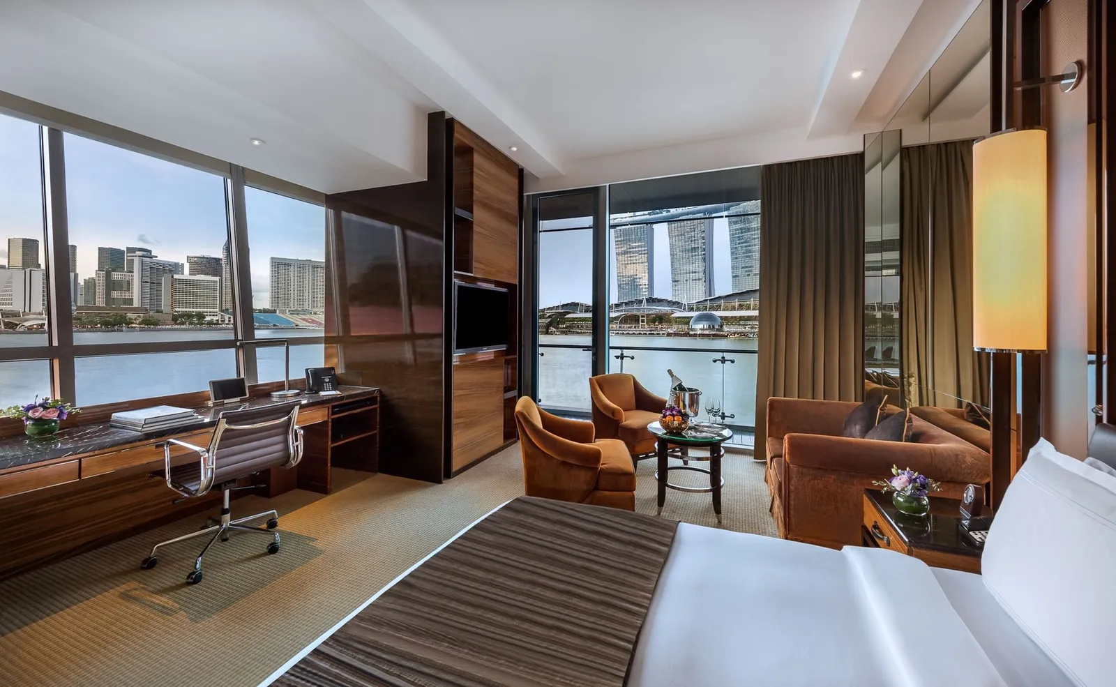 A Bay View Corner Room: the desk, armchairs and sofa between 2 walls of windows, with the towers across the bay.
