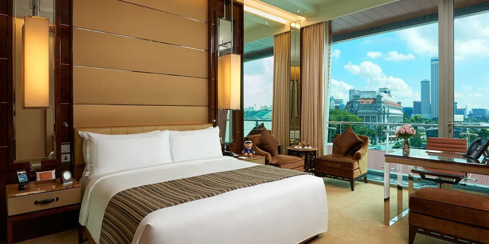 A Premier Room: the king bed, 2 armchairs and the desk in front of floor-to-ceiling windows onto the city.