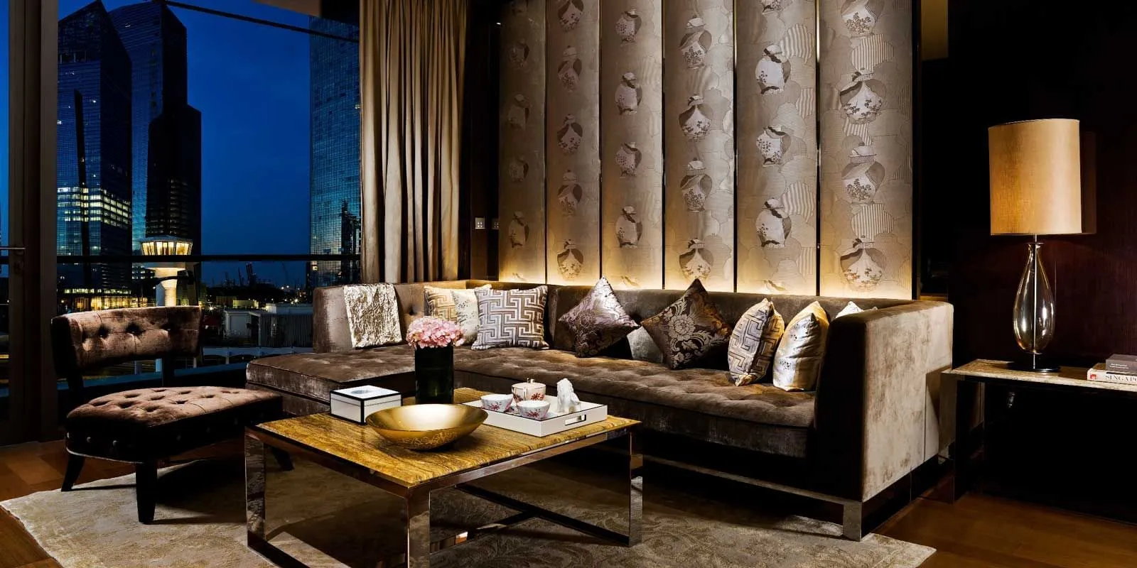 The Cavenagh Suite’s living room: a long sofa, padded wall panels and the towers at dusk through the window.
