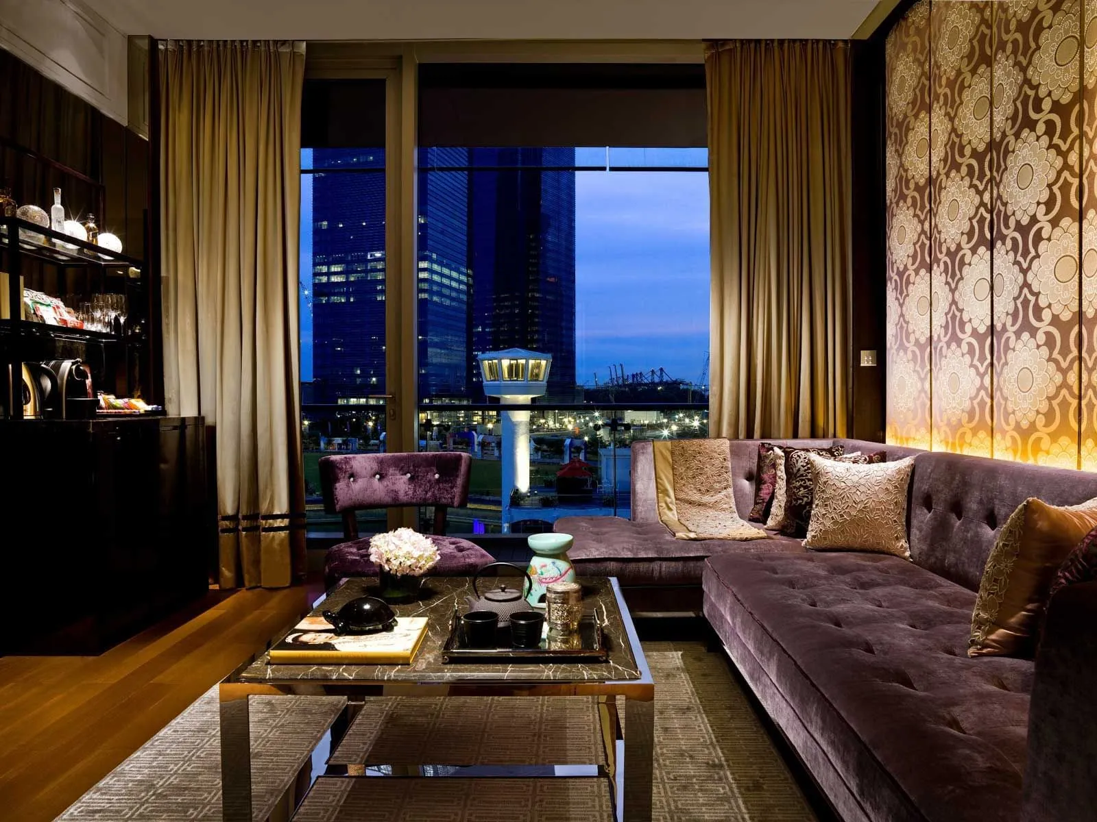 The Anderson Suite’s living room: a buttoned purple sofa, a glass coffee table and the city at night through the window.