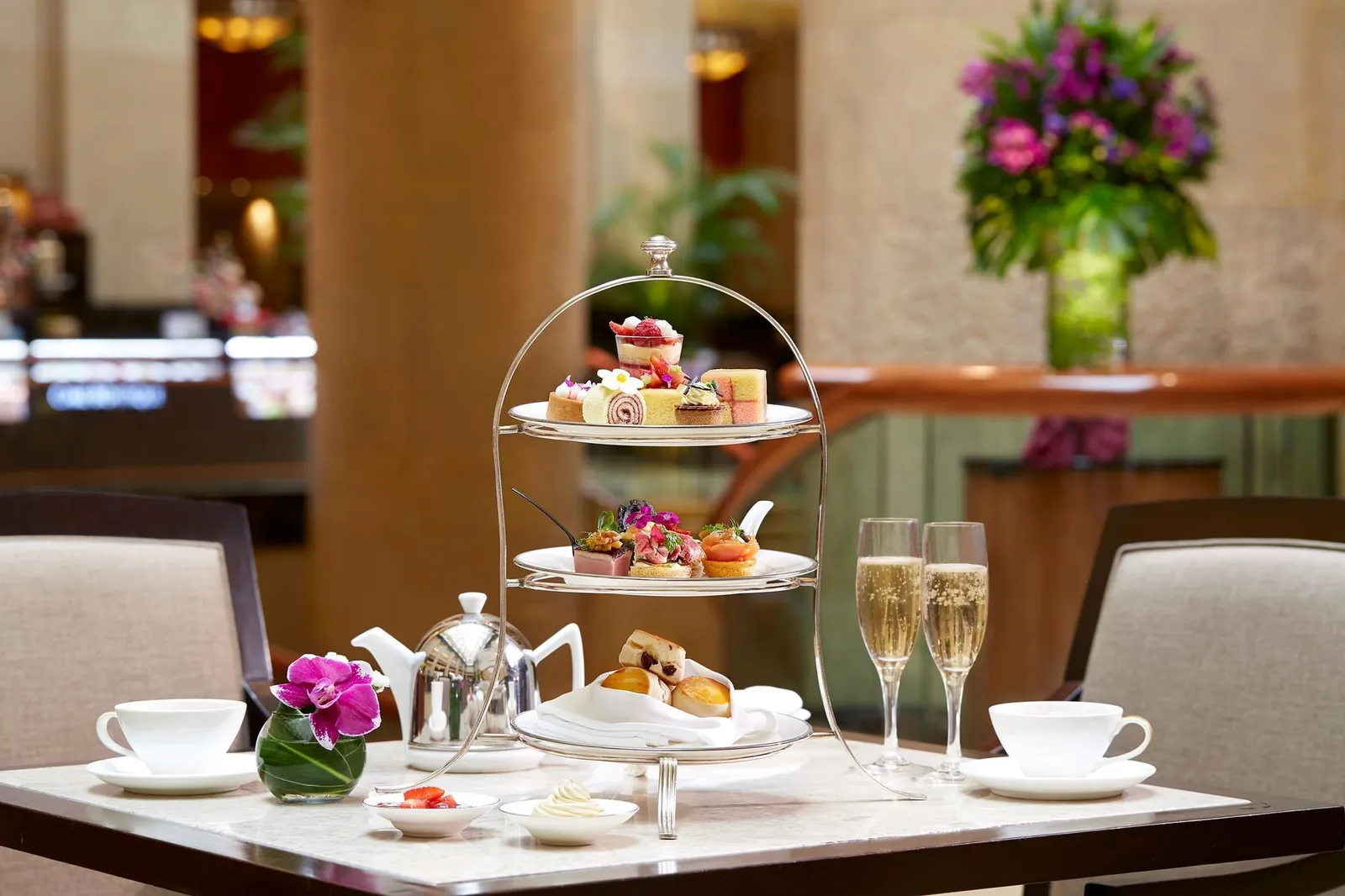 Un’alzata di dolci e tramezzini per il tè, 2 calici di champagne e una teiera su un tavolo di marmo a The Courtyard