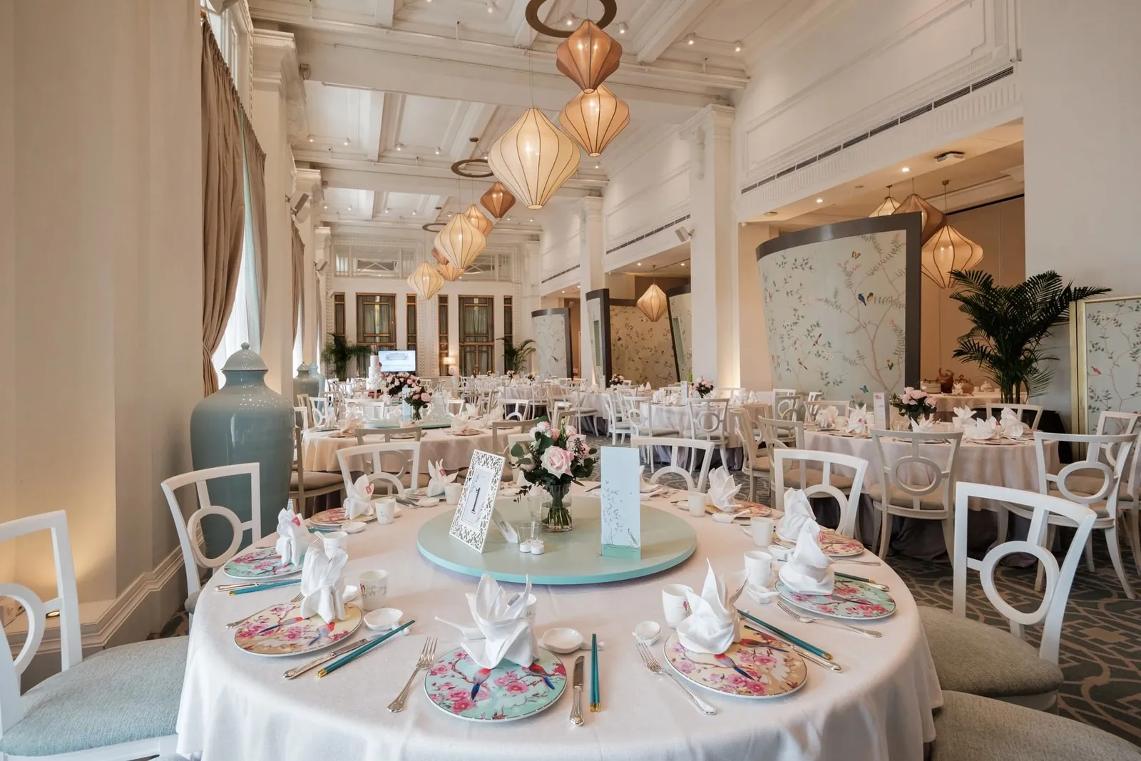 La sala di Jade: tavoli rotondi con tovaglie bianche e porcellane color pastello sotto lanterne di seta, un paravento dipinto e colonne alte