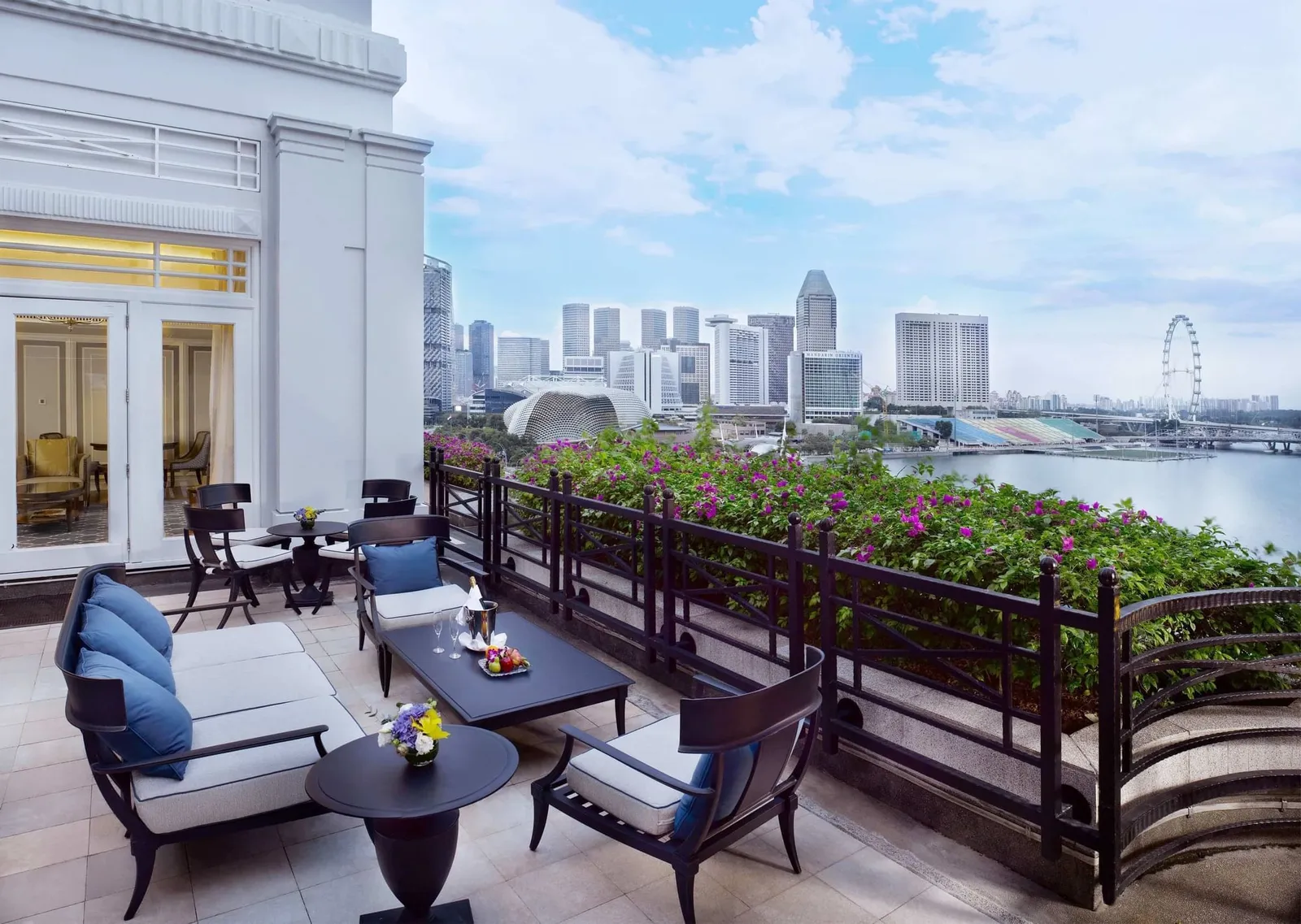 La terrazza della Fullerton Suite: divani con cuscini blu fra le bouganville, con Marina Bay e il Singapore Flyer sullo sfondo