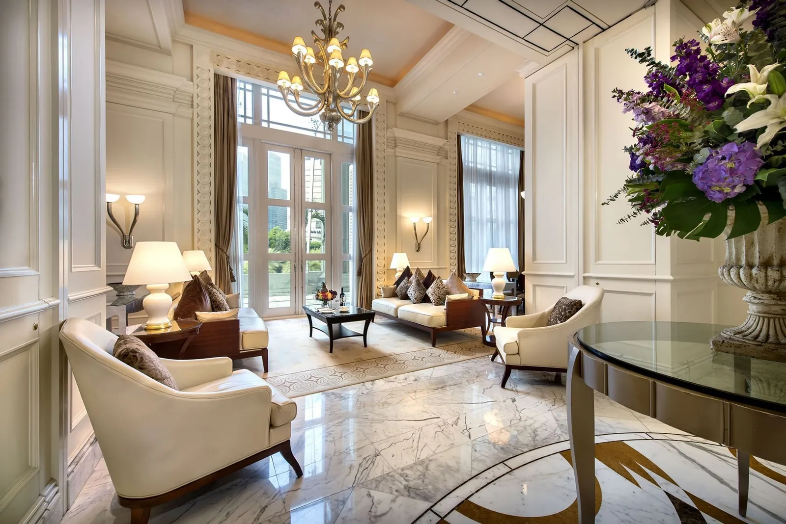 Il salotto della Presidential Suite: pavimento di marmo, poltrone color crema, un lampadario e un tavolo di vetro con le orchidee