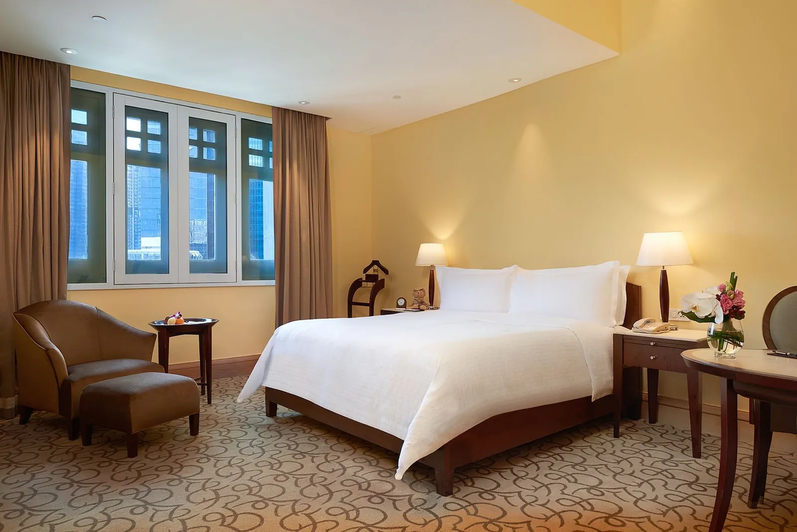 Una Straits Club Heritage Room: letto bianco, poltrona di pelle con poggiapiedi e finestre dalle persiane blu