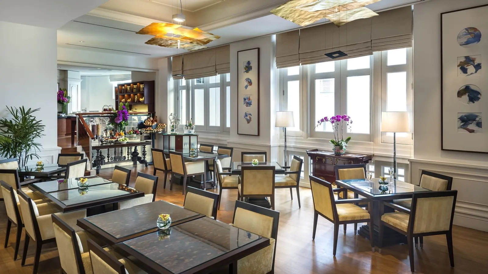 La lounge Straits Club: tavoli scuri e sedie color crema lungo una fila di finestre a ghigliottina, con orchidee sulle credenze