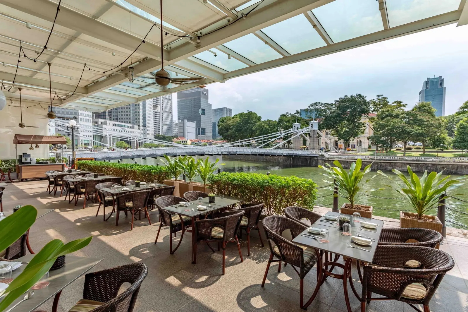 La terrazza coperta del Town Restaurant: sedie di rattan e tavoli apparecchiati lungo il fiume Singapore, con il Cavenagh Bridge sullo sfondo