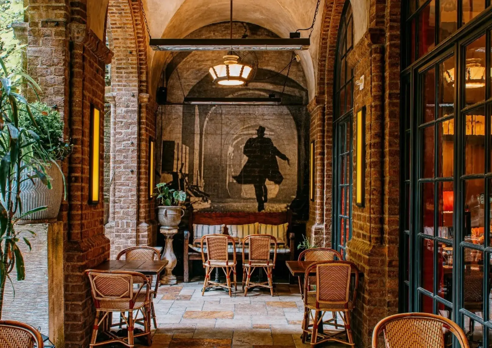 The Colonnade between brick arches, wicker chairs and the mural