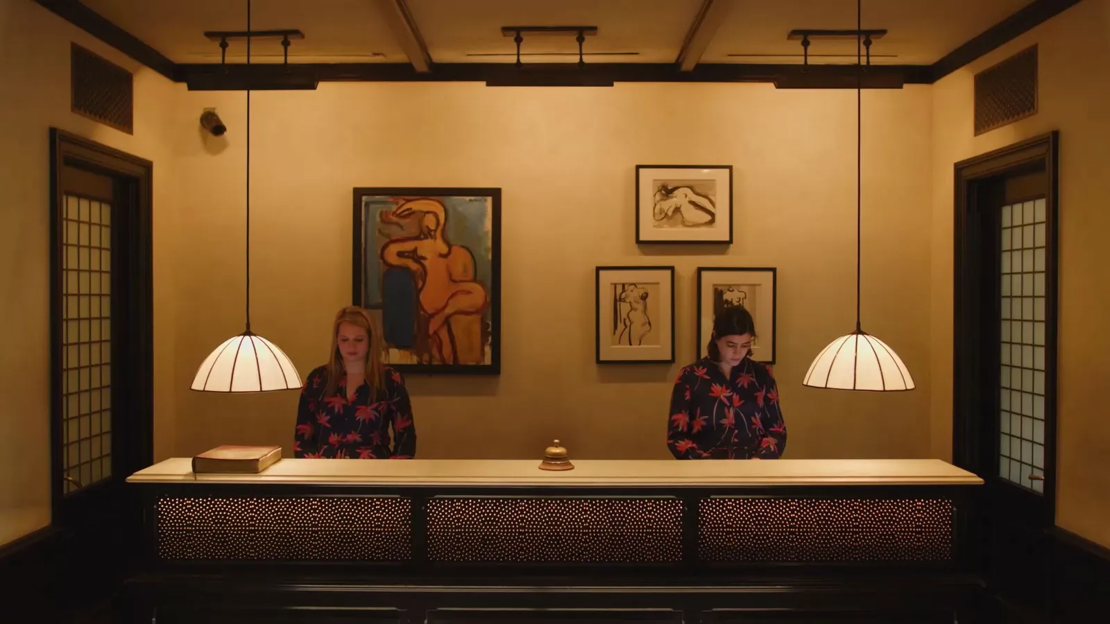 The front desk with its pendant lamps and paintings, 2 staff behind it