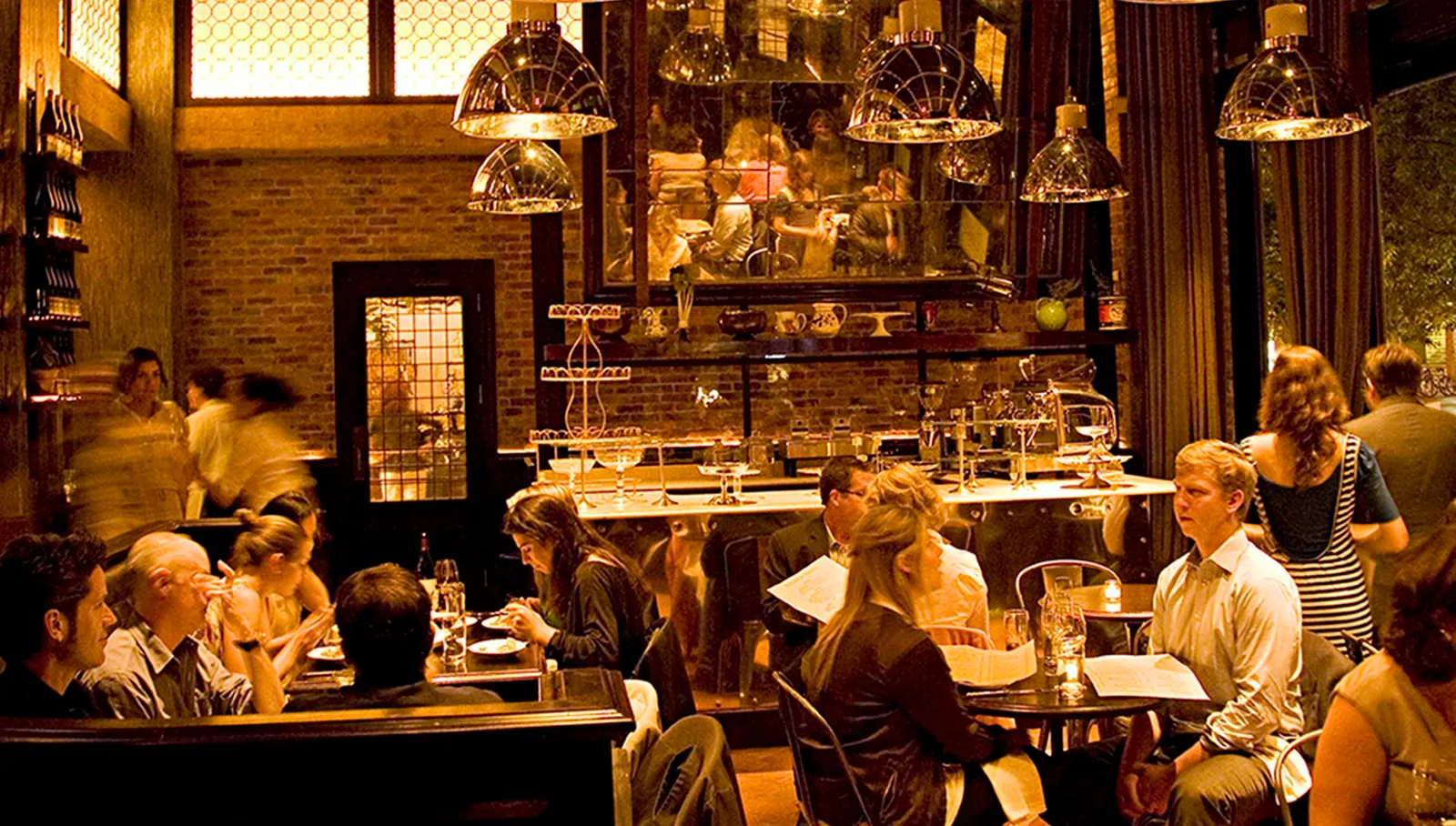 Locanda Verde’s dining room full of diners under the hanging lamps, the bar behind