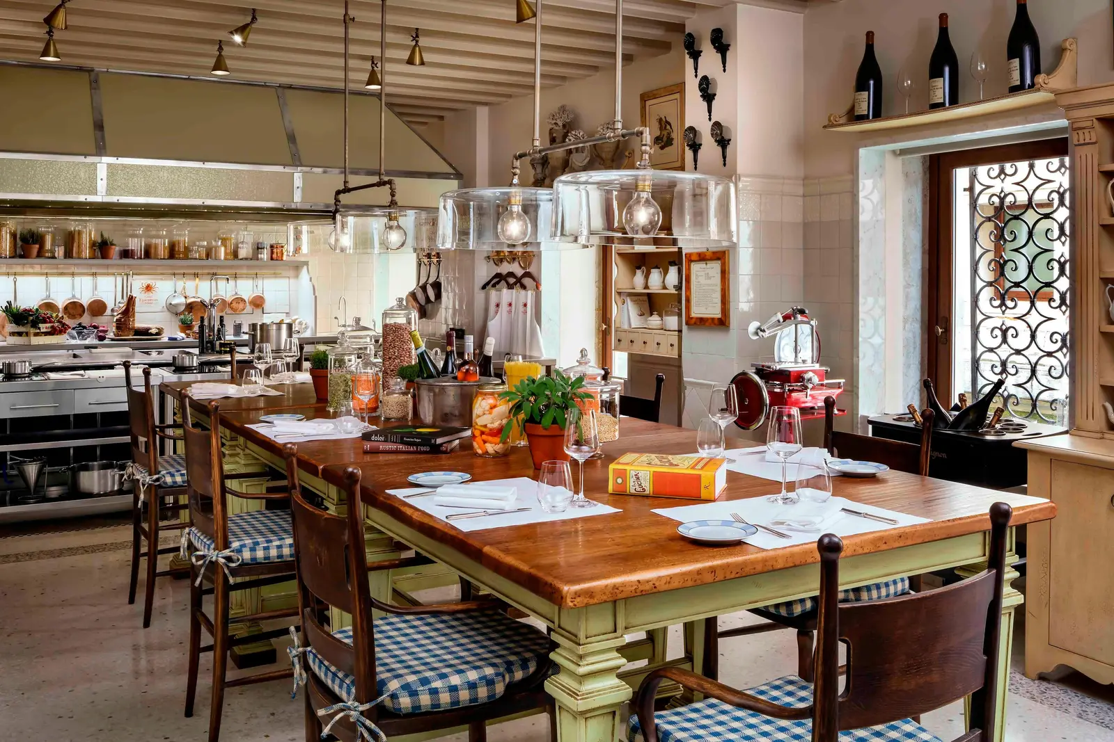 The Gritti Epicurean School kitchen: a long laid wooden table, hanging copper pans and a window with a wrought-iron grille.