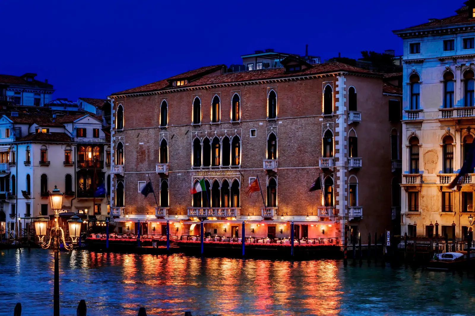The palazzo’s Gothic façade seen from the Grand Canal at night, its lit windows and terrace reflected in the water.