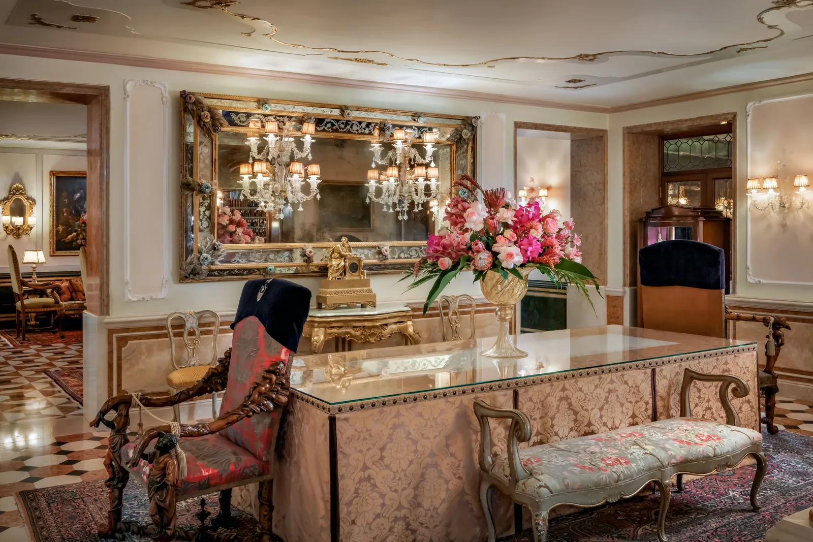 The lobby: the damask-clad reception desk, a large Venetian mirror, a spray of pink flowers and a chequered marble floor.