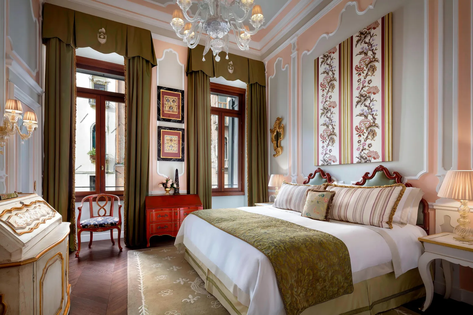 A Giglio Prestige room: the king bed between 2 tall windows with green curtains, floral fabric panels and a lacquered bureau.