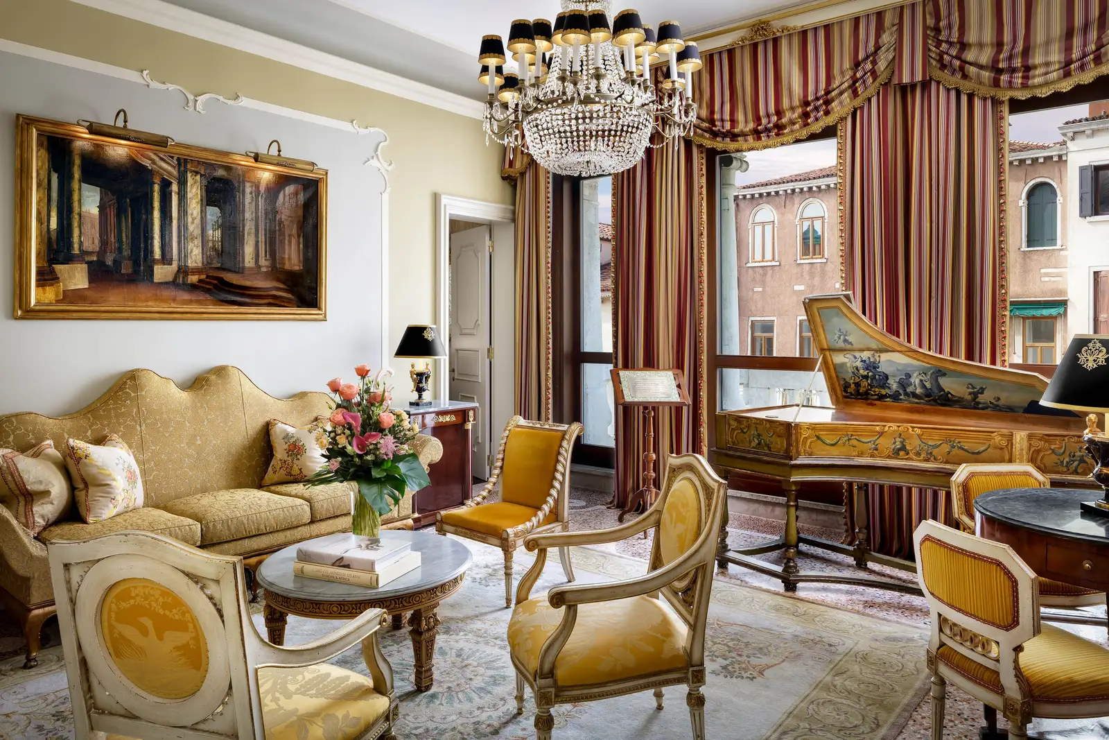 The sitting room of the Heritage Suite named after La Fenice: a painted harpsichord, gilt armchairs, striped curtains and a crystal chandelier.