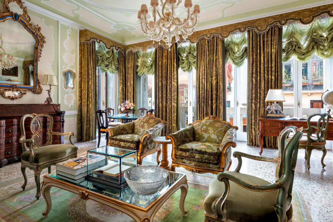 The Presidential Suite sitting room: green brocade armchairs around a glass table, gold curtains and French windows onto the Grand Canal.