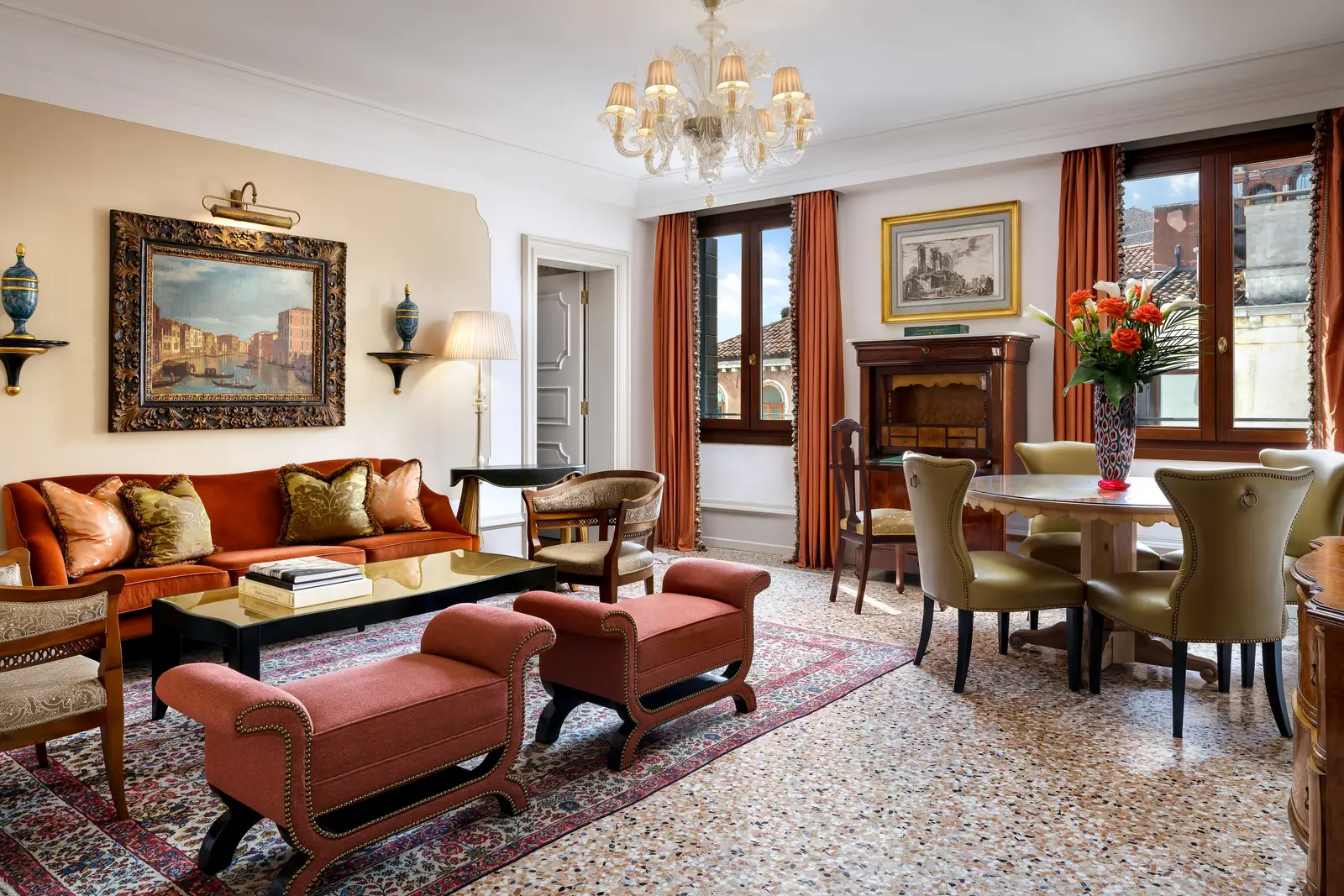 A Serenissima Suite sitting room: brick-red sofa and benches, a round dining table and 2 windows onto the campo.