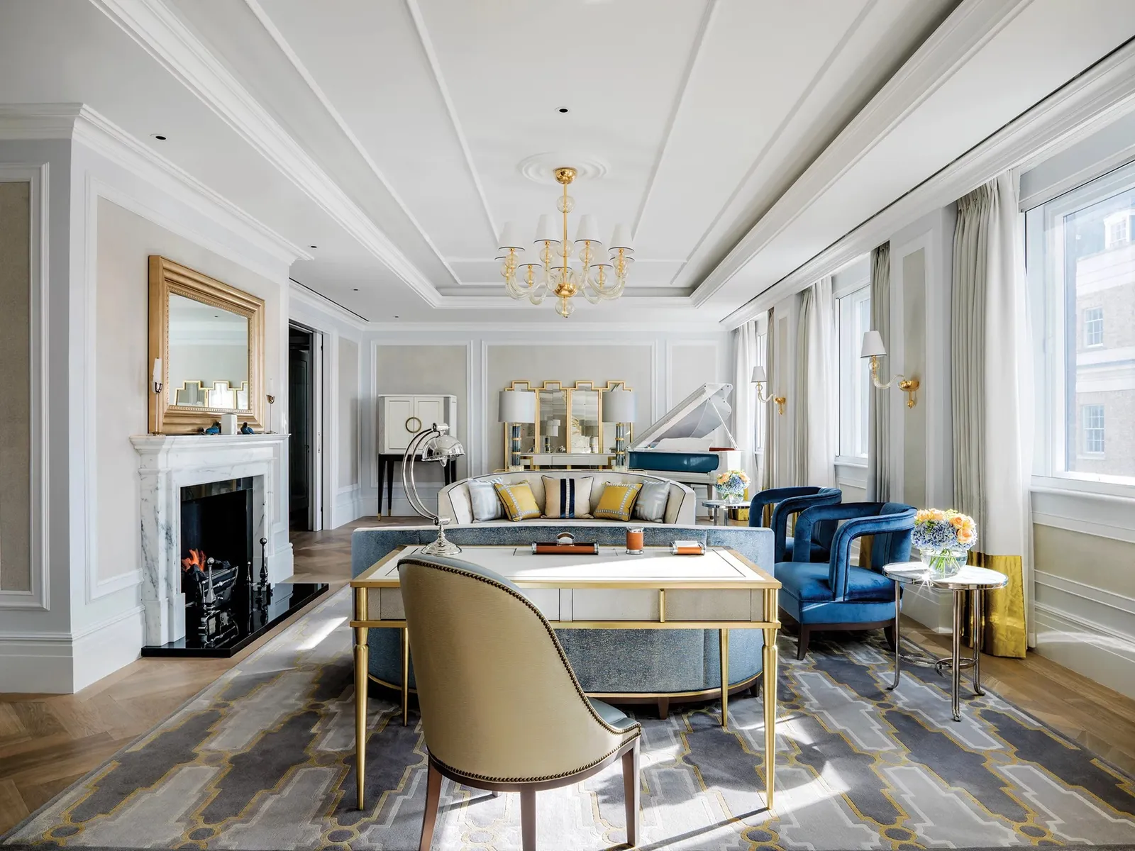 The Sterling Suite’s drawing room: a marble fireplace, a chandelier, a gilded desk and blue sofas