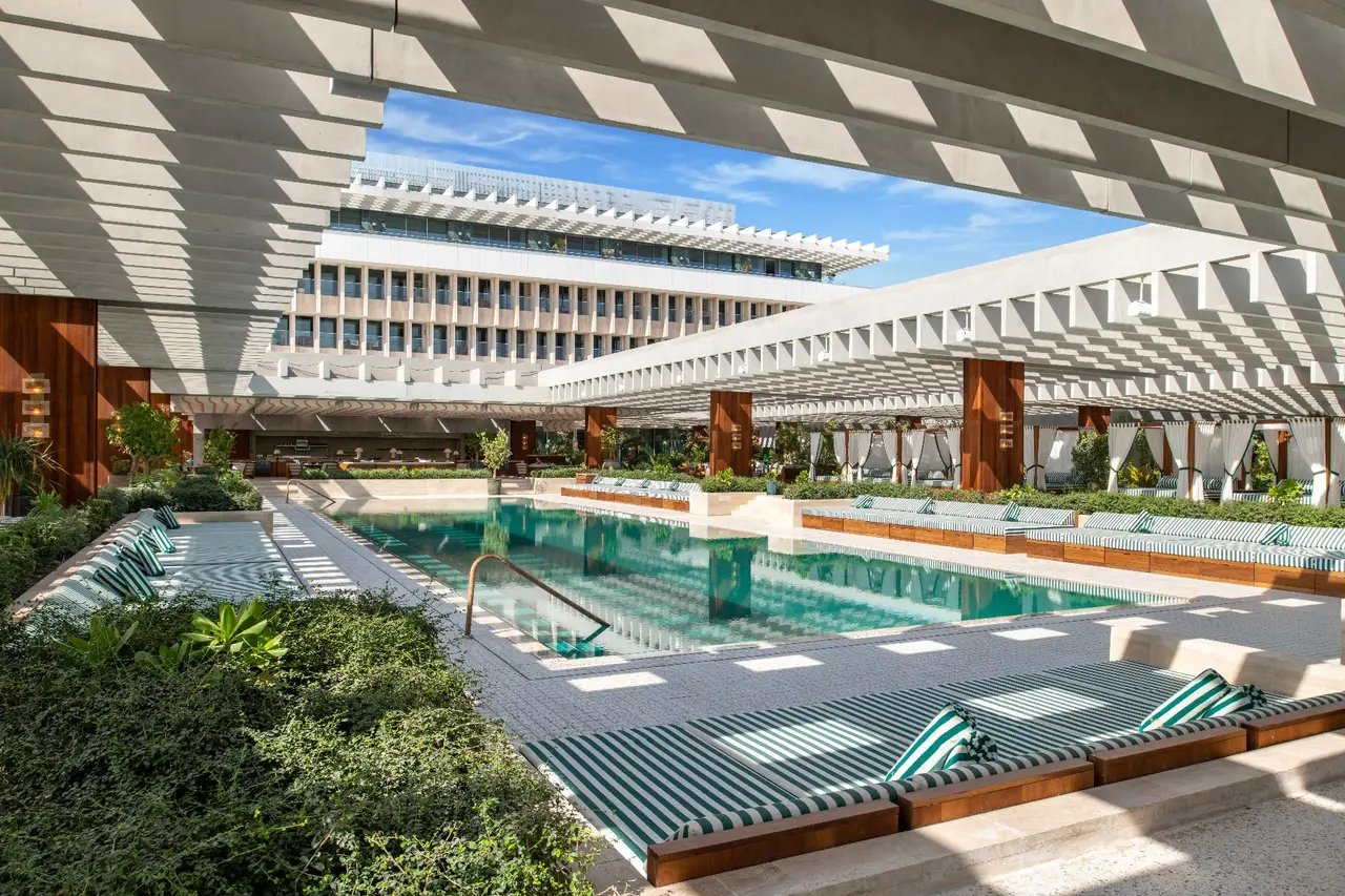 The long pool with green-and-white striped loungers, under the concrete façade