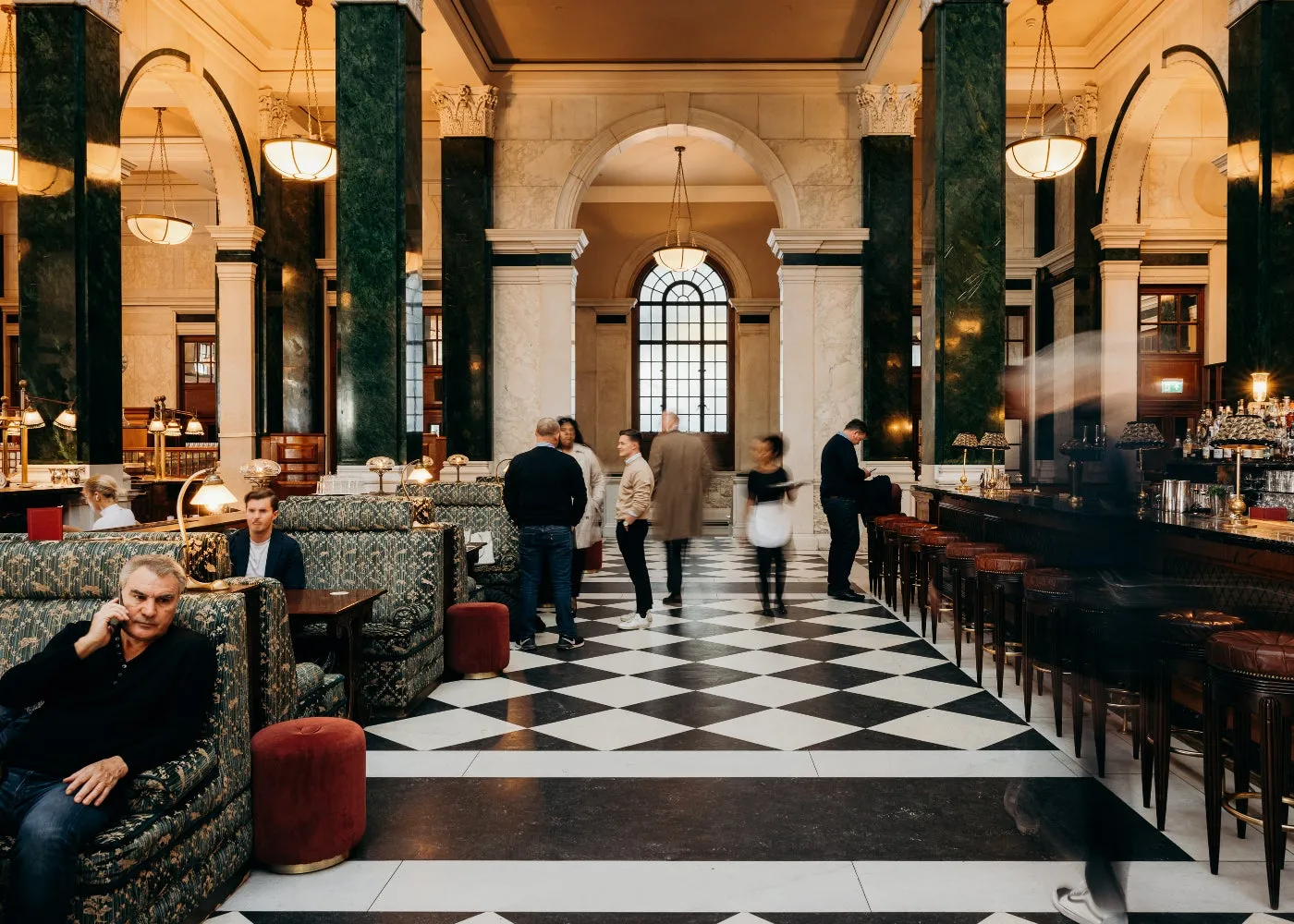 The Nickel Bar in the hall: a black-and-white chequered floor, the counter and verdite columns, people seated and passing through