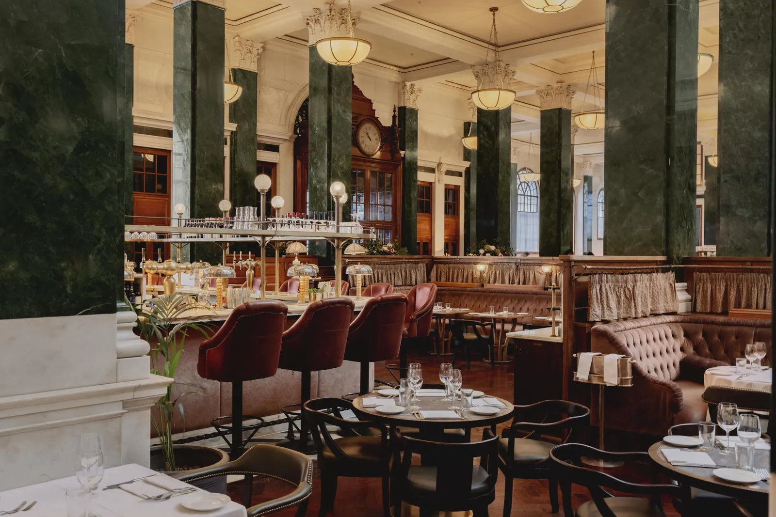 Cecconi’s in the banking hall: red stools at the counter, laid tables, green marble columns and tall windows