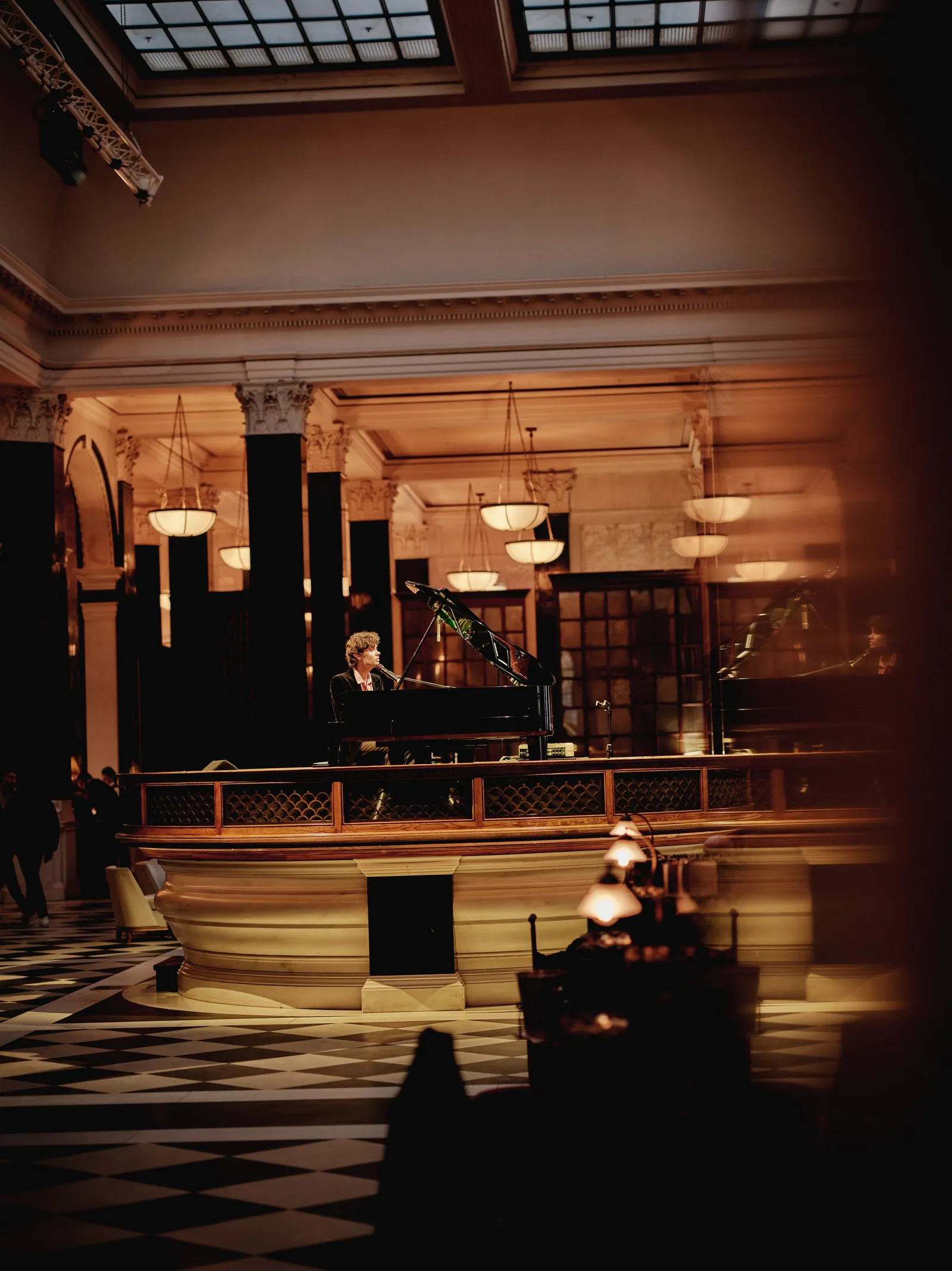 A pianist on the Nickel Stage in the middle of the hall, lit among tables in half-light