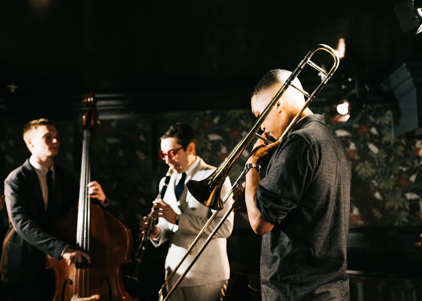 3 jazz musicians, double bass, clarinet and trombone, play before a dark wall