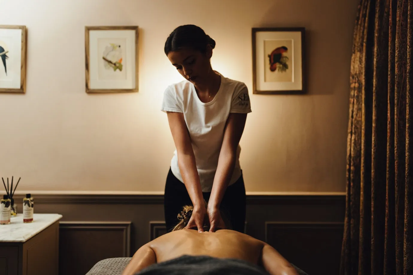 A therapist massages a guest’s back in a cream-walled treatment room