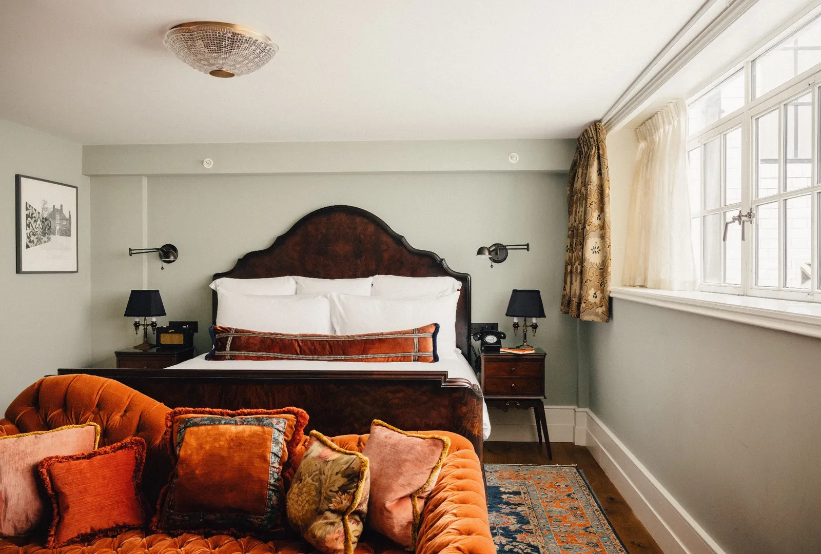 A Stairwell Studio: a bed with a dark wooden headboard, an orange velvet sofa and a bright window