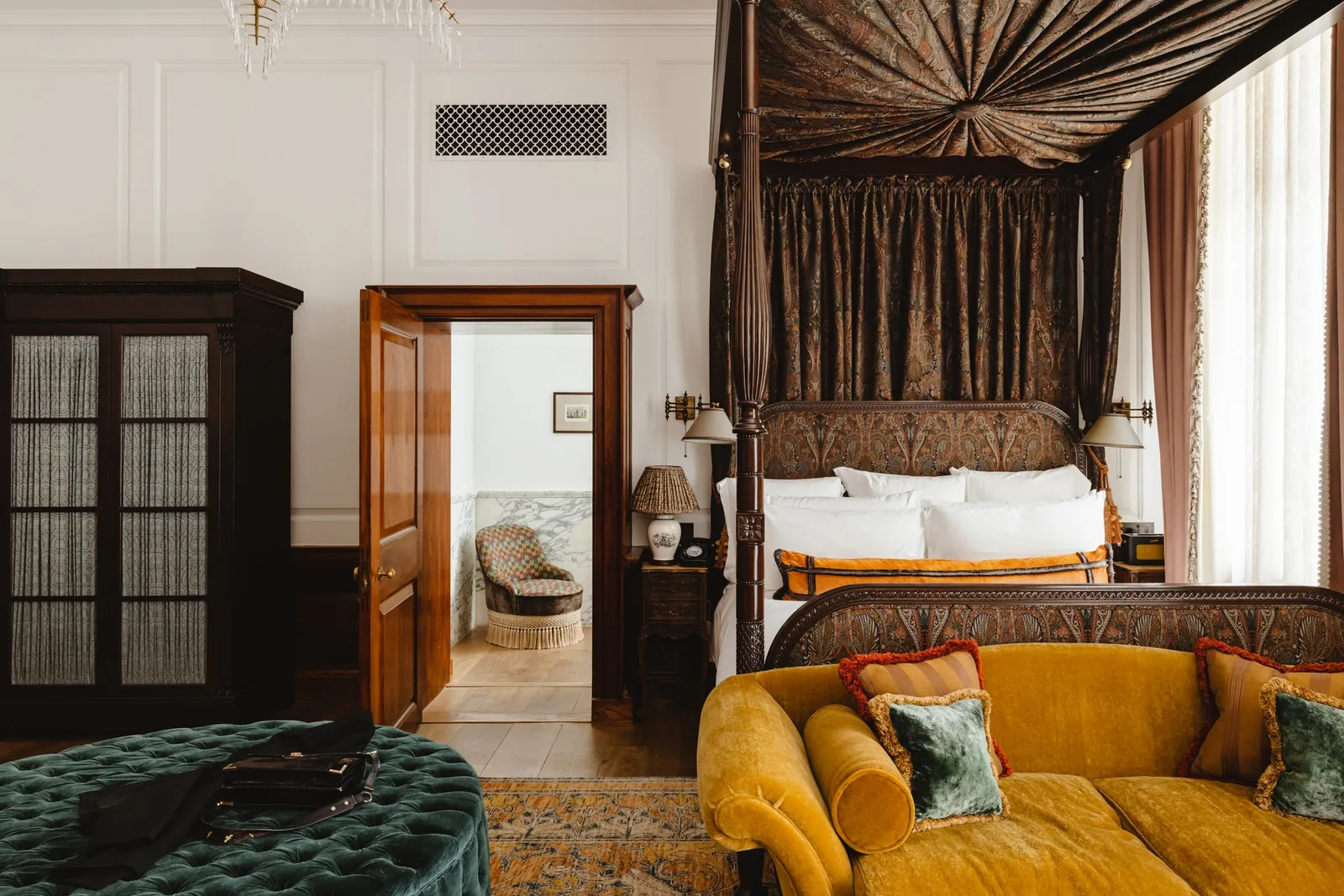 The Terrace Suite: a draped four-poster bed, a mustard velvet ottoman and a door through to the bathroom
