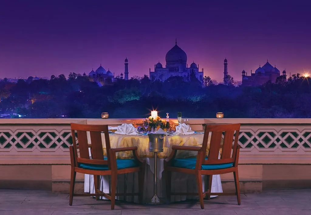 A table for 2 on a room’s balcony, with the Taj Mahal lit at dusk