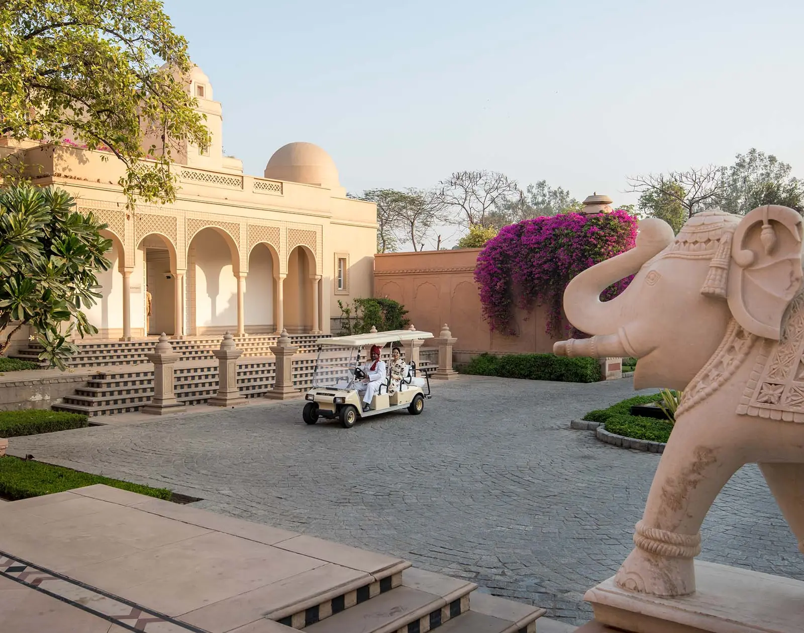 A golf cart in the entrance court, between a stone elephant and the bougainvillea