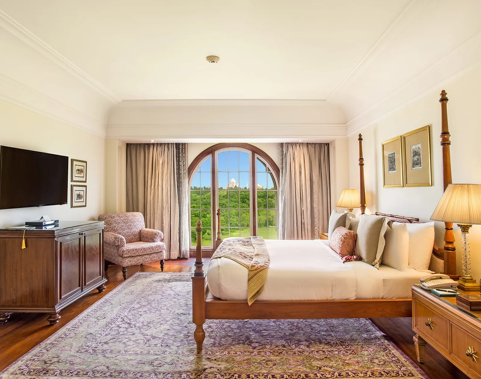 A Luxury Suite’s bedroom with its four-poster bed and the arched window onto the Taj Mahal
