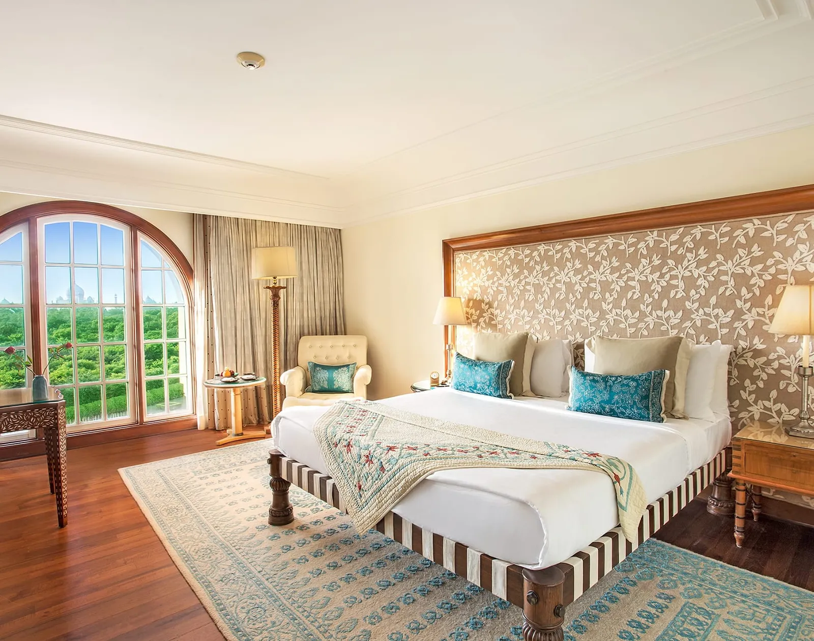 A Premier Room with its king bed and arched window onto the woods, the Taj Mahal in the distance