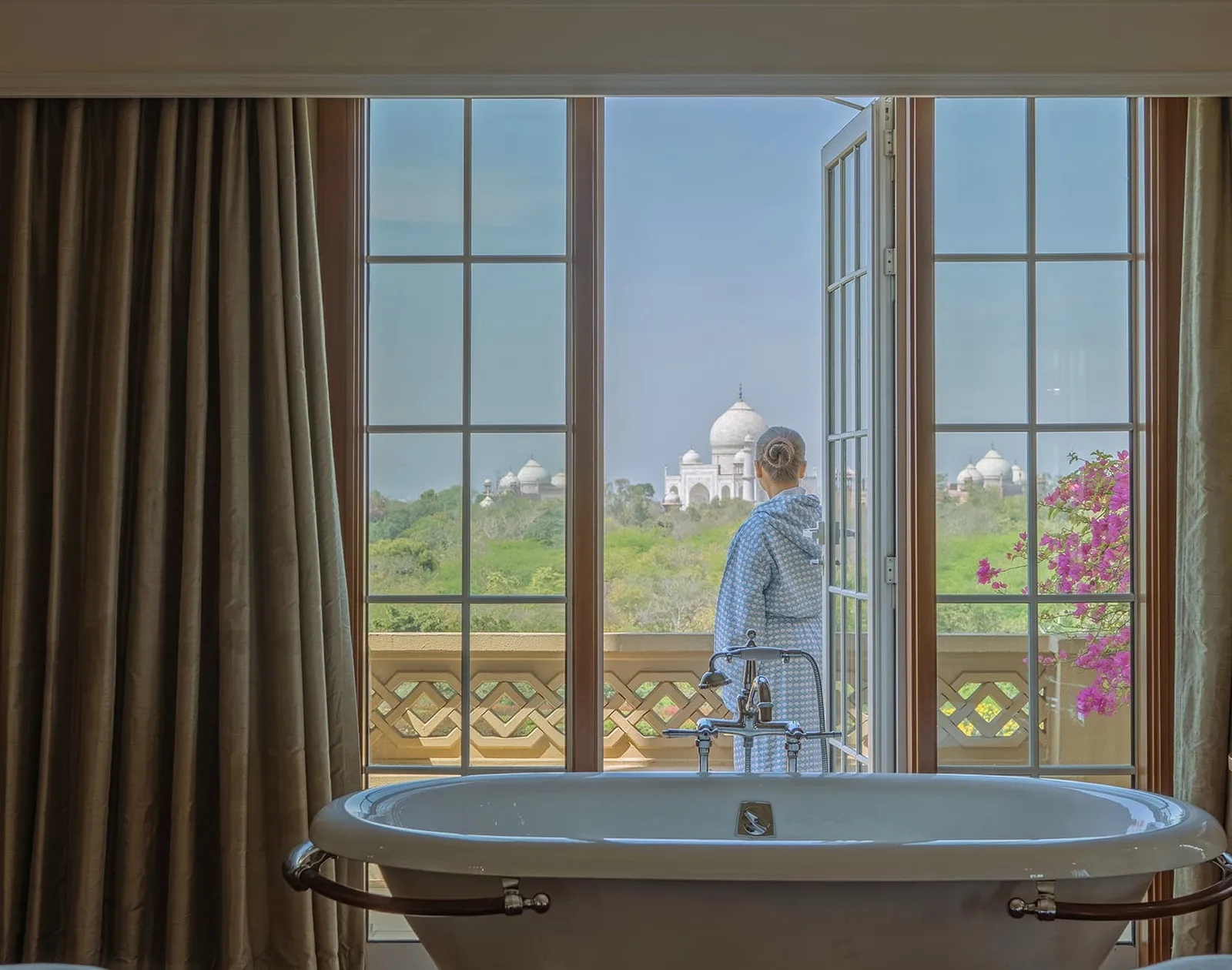 A guest in a robe at the spa’s window, the bath before her and the Taj Mahal in the distance