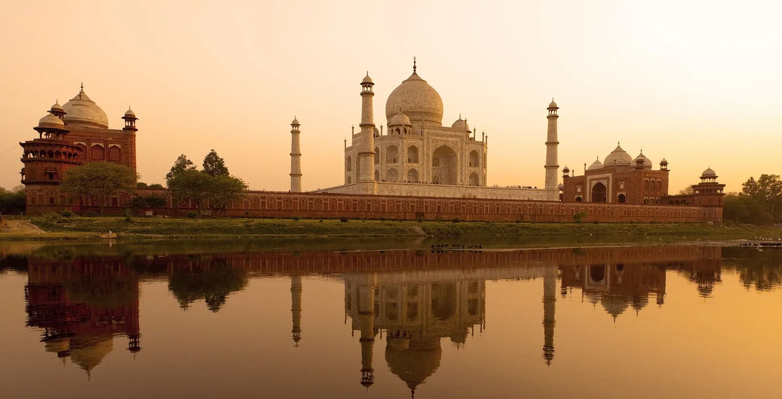The Taj Mahal at sunset, reflected in the Yamuna, a red sandstone mosque to the left