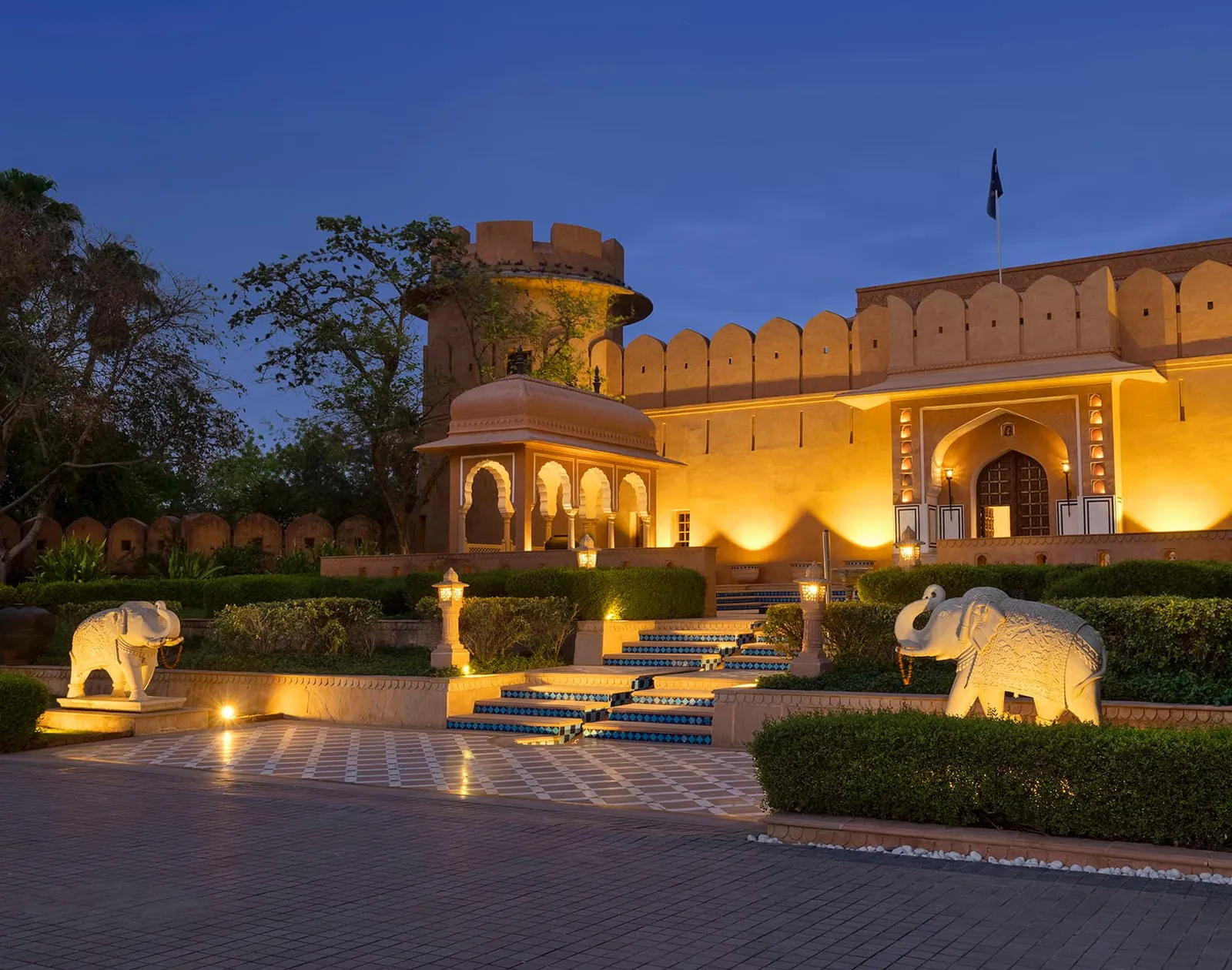 The resort’s entrance at dusk, its pink walls lit and 2 stone elephants at the steps