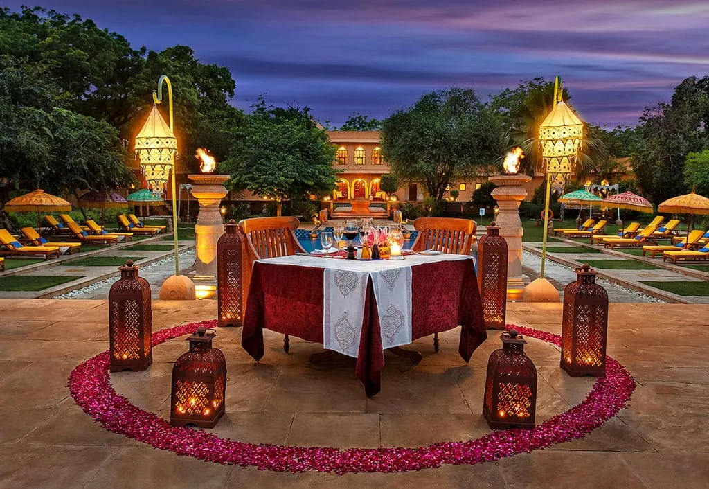 A table for 2 by the pool, among lanterns and rose petals, at dusk