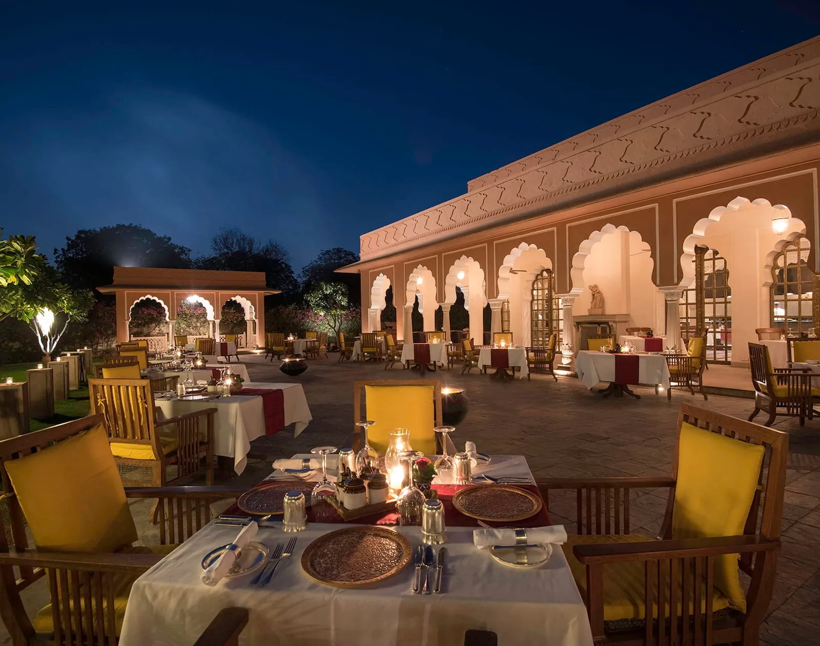 Tables laid in Raj Mahal’s courtyard at night, beneath lit arches