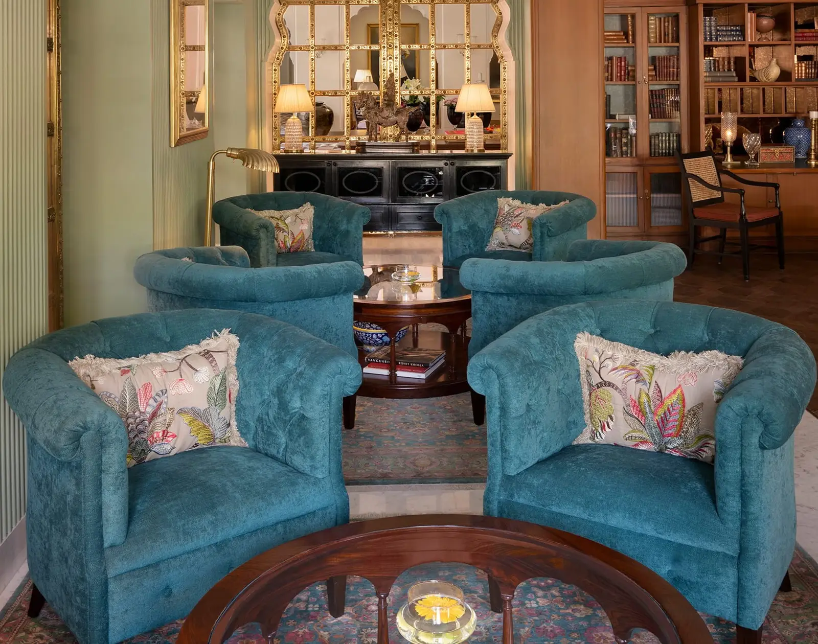 Peacock-blue armchairs round a low table in the Rajwada bar, between bookshelves