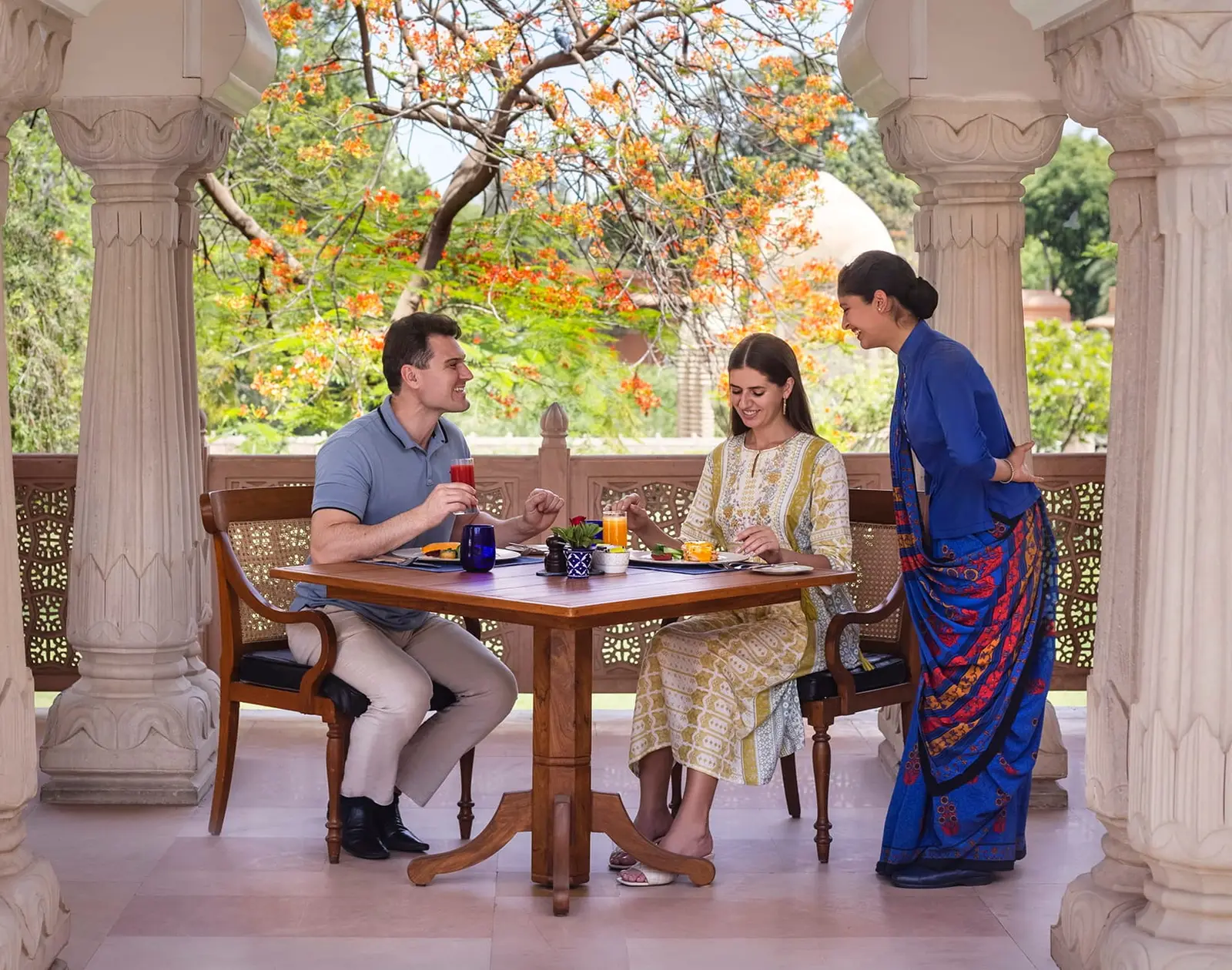 A couple at table beneath Surya Mahal’s arches, served by a waitress in a blue sari