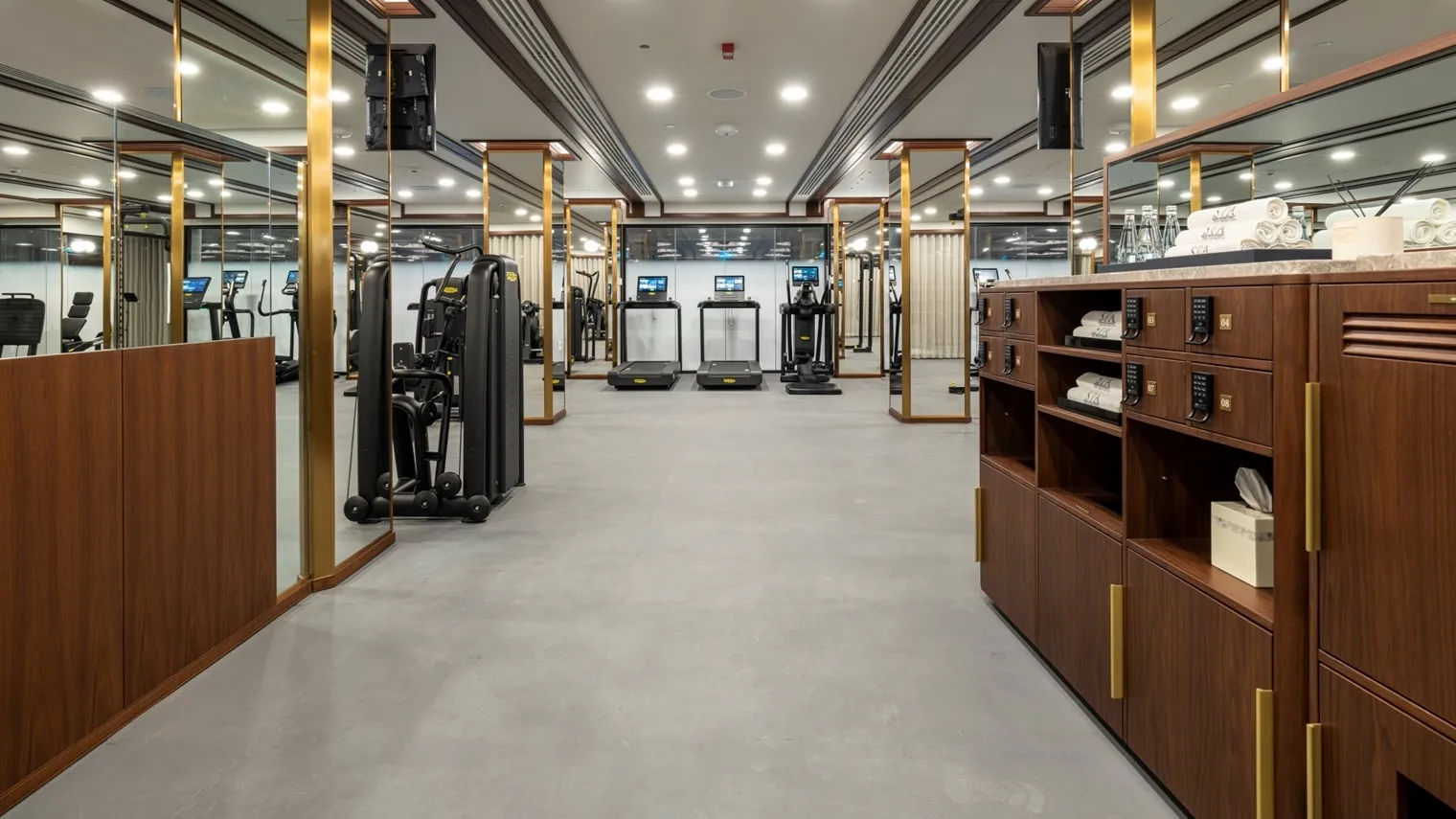 The gym: treadmills and machines down the room, mirrors framed in brass and a wooden unit stocked with towels.