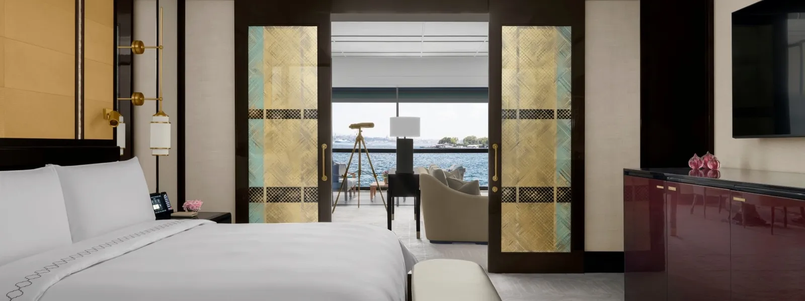 A Deluxe Bosphorus Suite with Balcony: the bed in the foreground and, through sliding doors with gilded panels, the living room with a telescope at the window on the Bosphorus.
